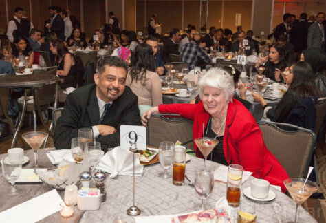 A man and a woman smile from their banquet table in a hall of tables.