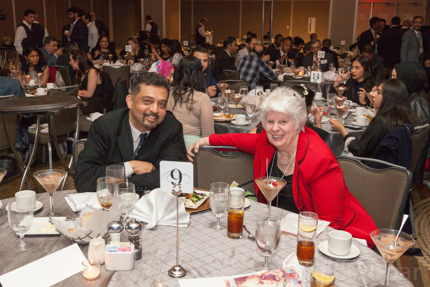 A man and a woman smile from their banquet table in a hall of tables.