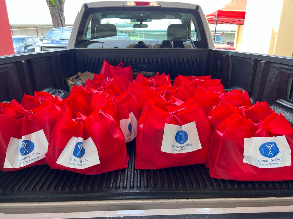 The bed of a pickup truck is filled with red canvas bags bearing the humanity first logo. The bags are full of supplies and tied closed.