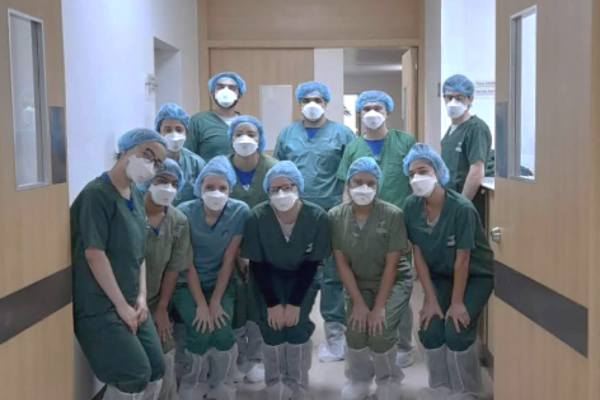 A dozen people post in a group in a hallway wearing green surgical scrubs, hair coverings, and white masks.
