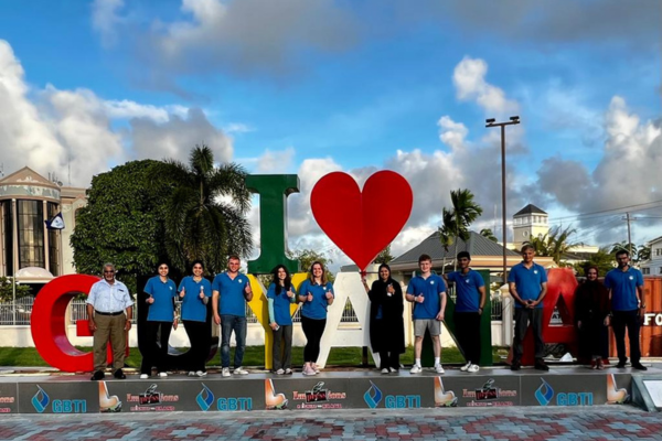 Students from the Gift of Health medical mission wear blue Humanity First polo shirts and stand in a line in front of a large sculpture that reads I heart Guyana.