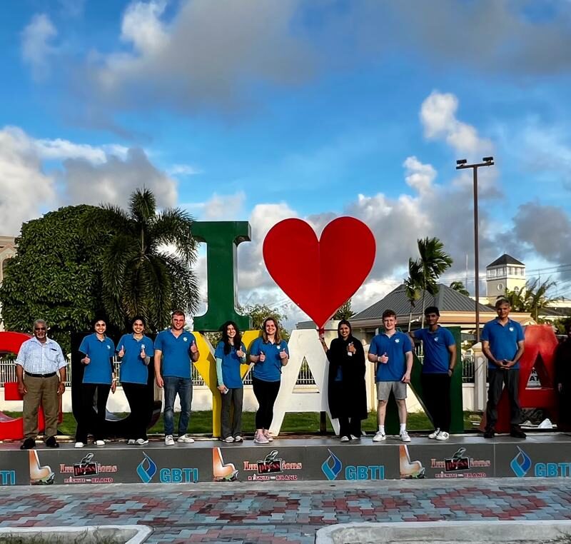 Students from the Gift of Health medical mission wear blue Humanity First polo shirts and stand in a line in front of a large sculpture that reads I heart Guyana.