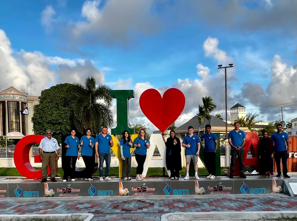 Students from the Gift of Health medical mission wear blue Humanity First polo shirts and stand in a line in front of a large sculpture that reads I heart Guyana.