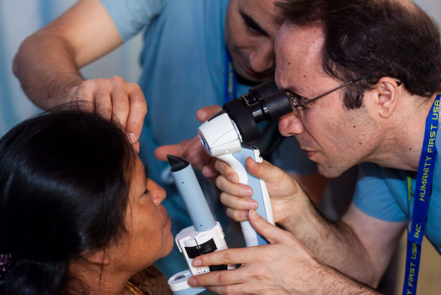 Two doctors using a device to look into a patient's eyes.