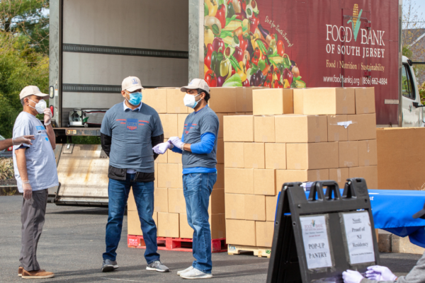 A food bank truck is parked behind stacks of unloaded cardboard boxes of food