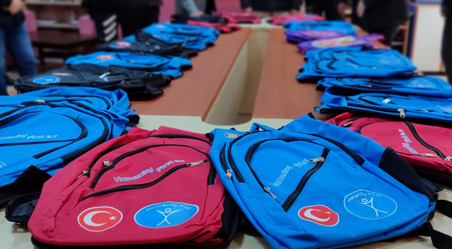 Dozens of brightly colored blue and red backpacks bearing the logos of Humanity First and the Turkish Red Crescent are displayed on a table.