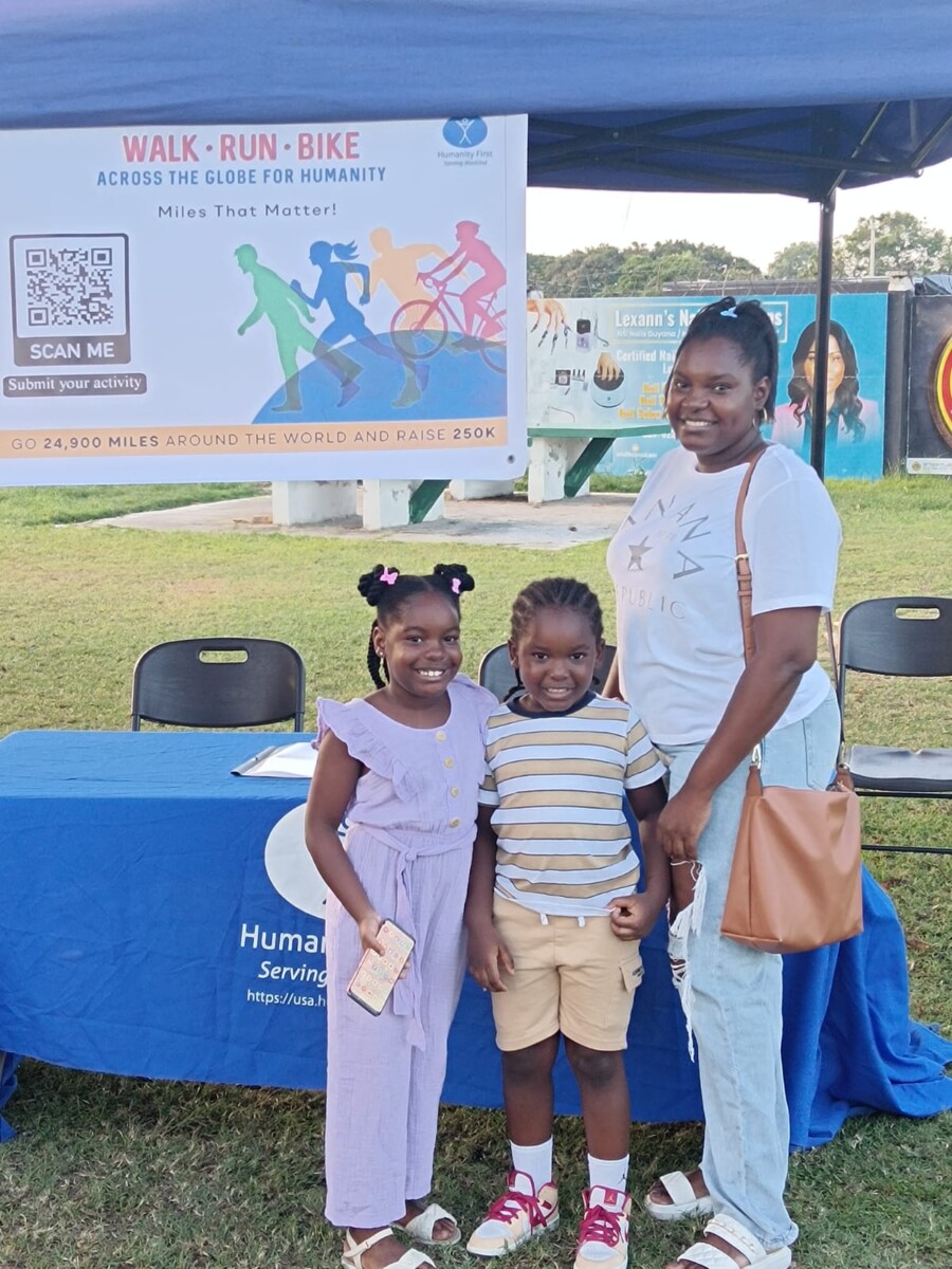 A mother and two children smile for the picture. They stand in front of an outdoor tent awning and a side for walk run bike event.