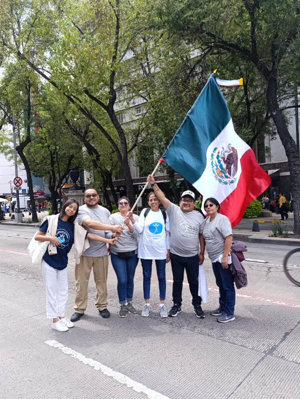 six people stand in a street holding a giant flag of Mexico