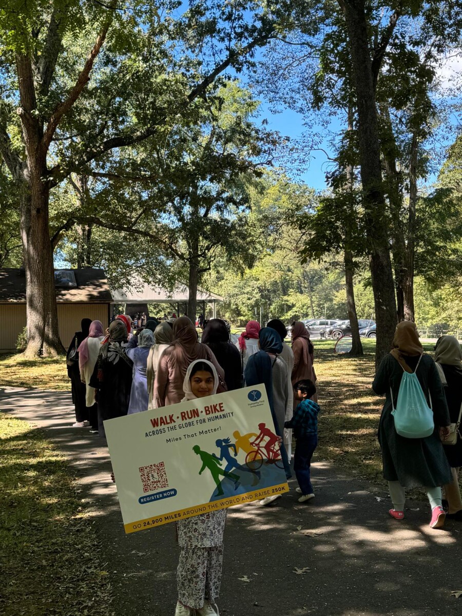 A young girl wearing a headscarf holds a sign reading walk run bike. behind her other girls and women are walking together