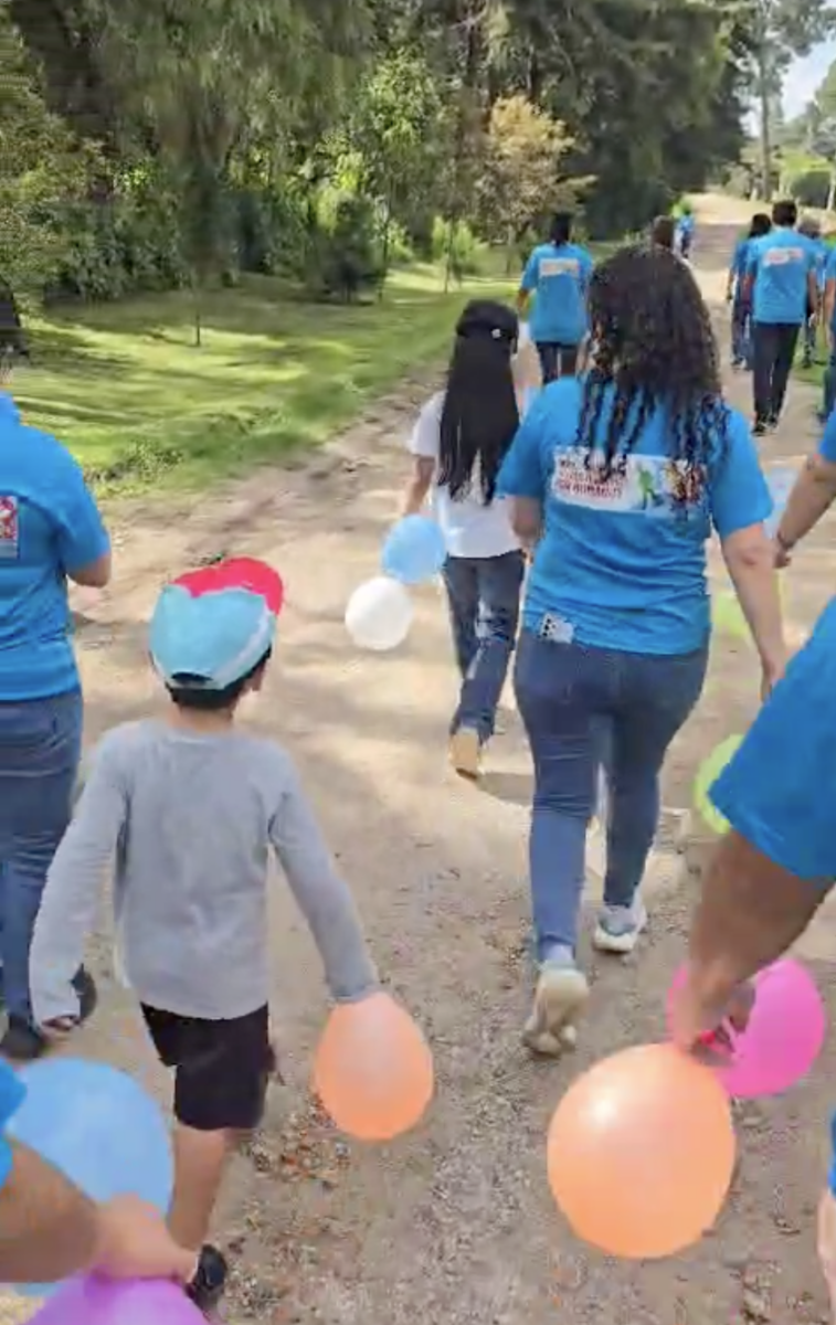 a group of adults and kids walks down a dirt path holding balloons. the adults wear matching bright blue t shirts.