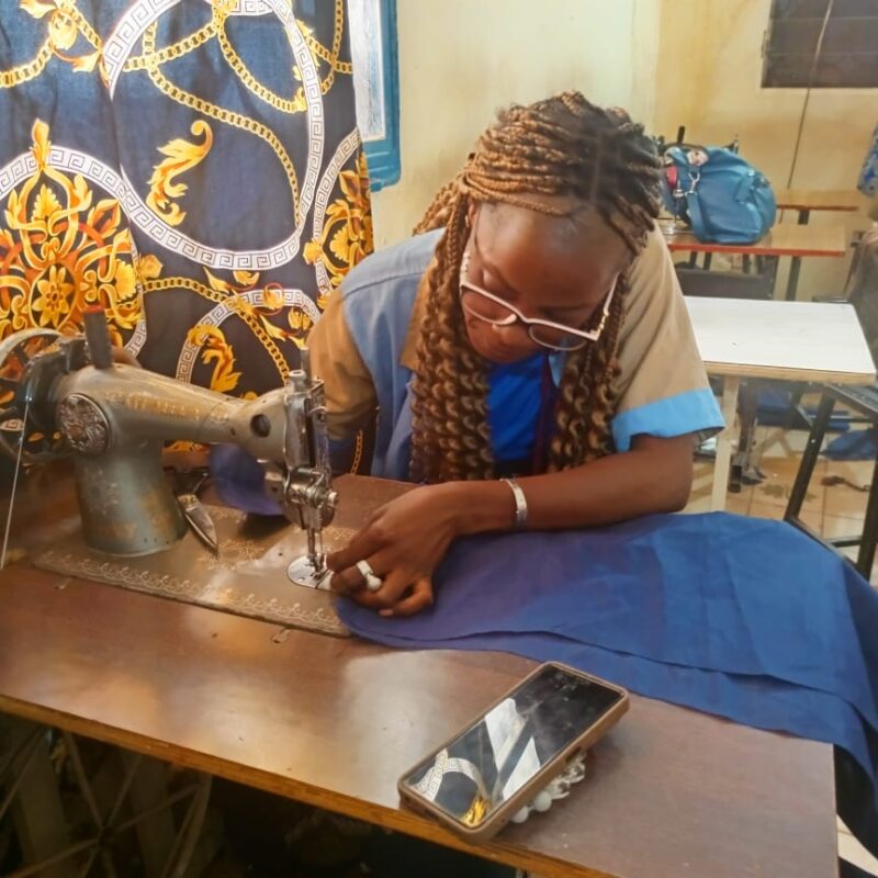 A woman threads her metal sewing machine to work on a deep blue colored cloth.