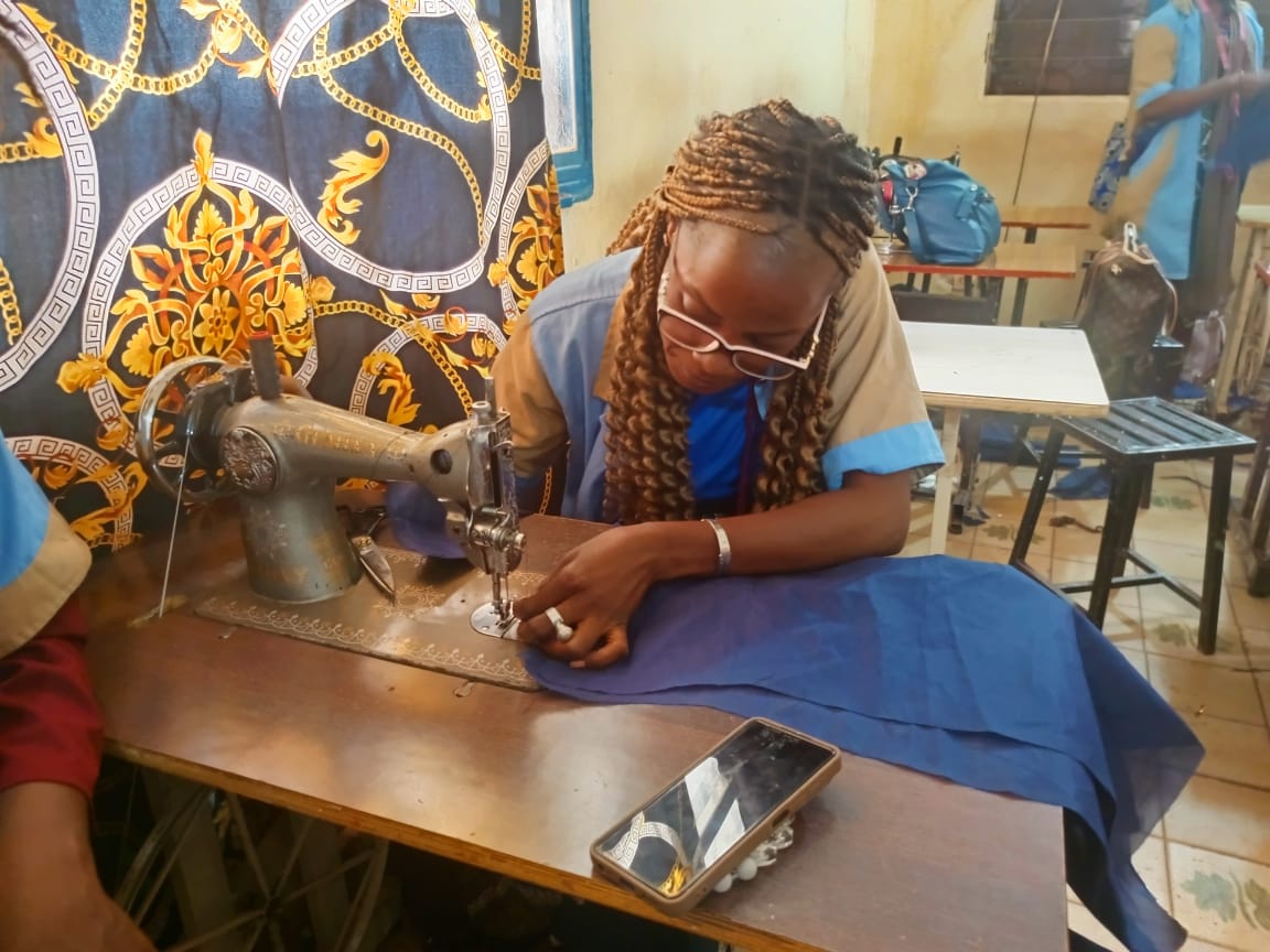 A woman threads her metal sewing machine to work on a deep blue colored cloth.