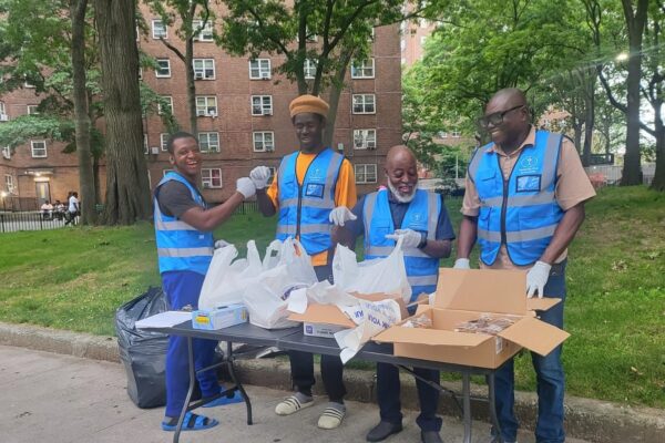 four men wearing HF blue vests stand behind a table stacked with bags and boxes of food