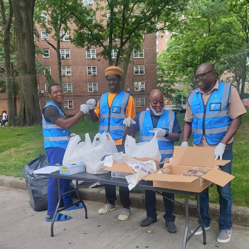 four men wearing HF blue vests stand behind a table stacked with bags and boxes of food