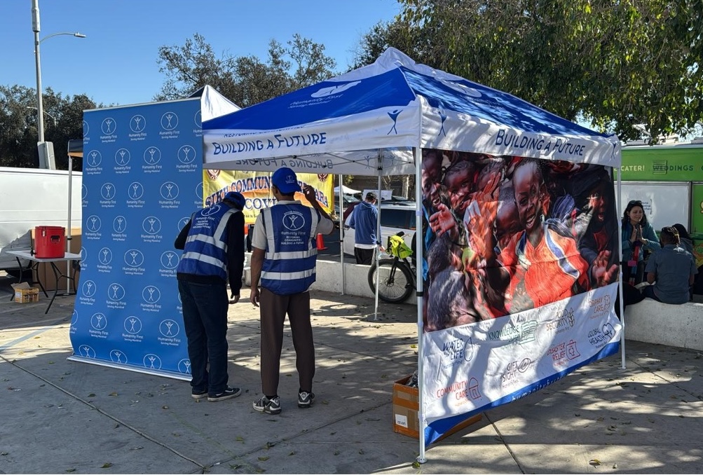 Men wearing blue humanity first vests set up a humanity first tent and banner in an outdoor space