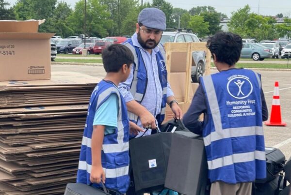 A man and two children wearing blue Humanity First vests carry small food coolers for relief donations.
