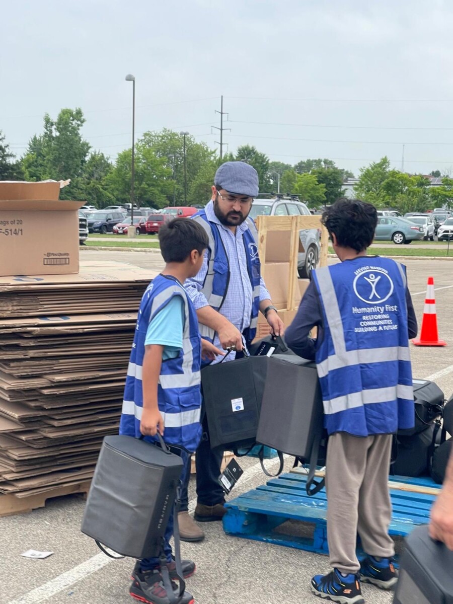 A man and two children wearing blue Humanity First vests carry small food coolers for relief donations.