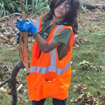 A child wearing a high visibility vest picks up small tree branches from a yard.